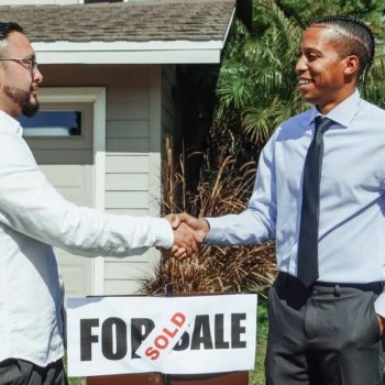 people shaking hands over a for sale sign