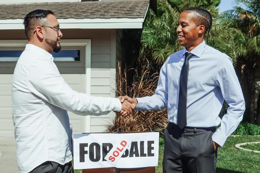 people shaking hands over a for sale sign